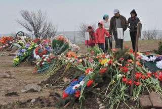 A Kyrgyz family stands opposite wreaths of flowers laid in the Ata-Beyit memorial ?complex outside Bishkek, to pay homage to the victims of April 7 clashes.?