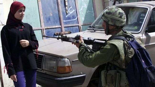 An Israeli soldier points his gun at a Palestinian woman in the occupied West Bank city of al-Khalil.