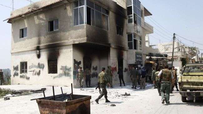 Syrian soldiers are seen near a burnt building in al-Haffeh village near Latakia.