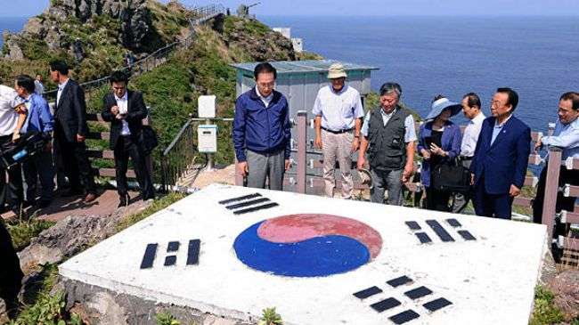 South Korean President Lee Myung-bak (c.) looks at a national flag upon his arrival at islands called Dokdo in Korea and Takeshima in Japan Friday, Aug 10, 2012.