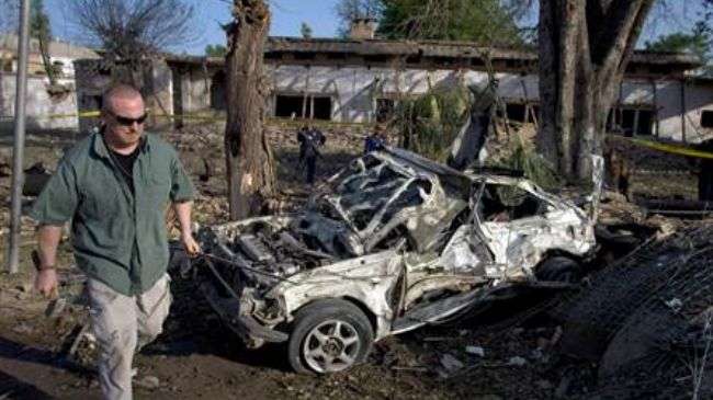 A US security official walks near a damaged car at the site of bombings near the US consulate in Peshawar, Pakistan, May 2011.