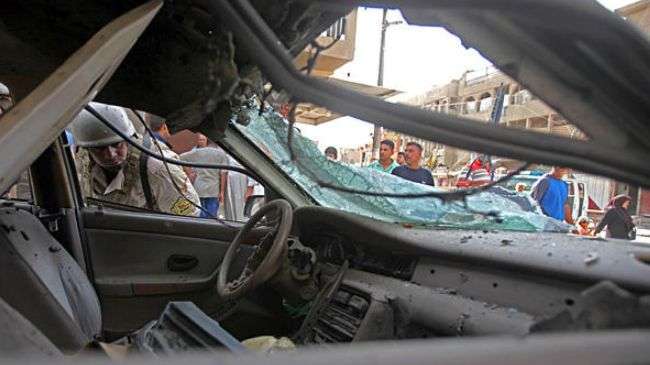 People inspect a destroyed vehicle after a bomb hidden under a car exploded in Baghdad