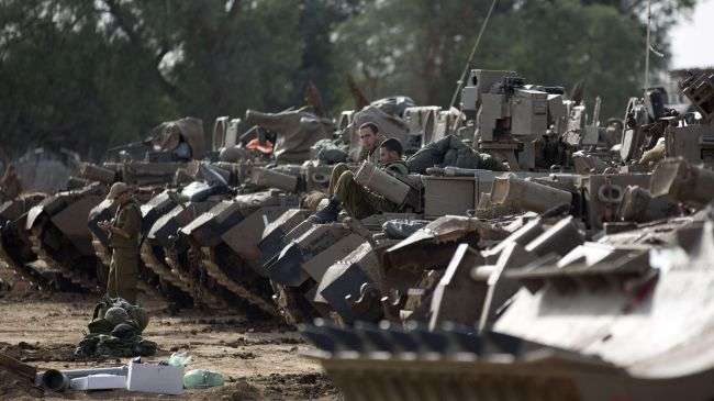 Israeli soldiers sit atop their armoured personnel carriers (APC) stationed on Israel