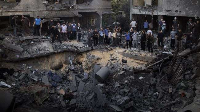 Palestinian men gather around a crater caused by an Israeli air strike on the al-Dallu family