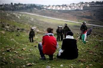 A Palestinian boy and woman sit as Israeli soldiers walk nearby during a protest against Jewish settlements, in Ramallah village Nabi Saleh, Jan. 11, 2013.