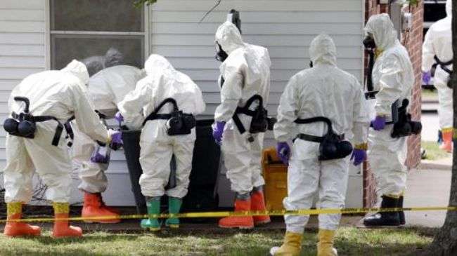 Federal agents wearing hazardous material suits and breathing apparatus inspect the trash can outside the West Hills Subdivision house of Paul Kevin Curtis in Corinth, Miss., Friday, April 19, 2013.