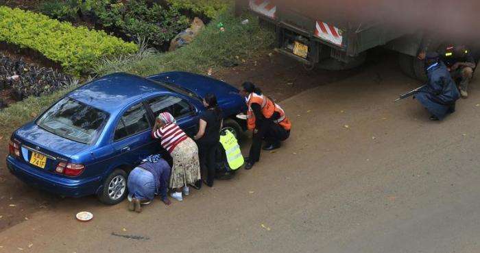People take cover behind their vehicles along a road during heavy gunfire at Westgate shopping centre in Nairobi September 23 2013.