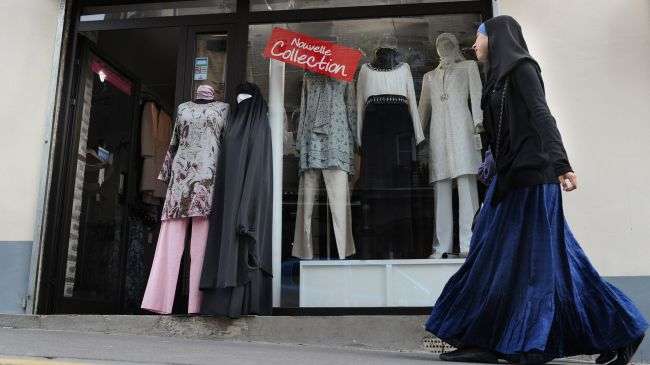 A woman wearing hijab walks past a shop in Paris, France.