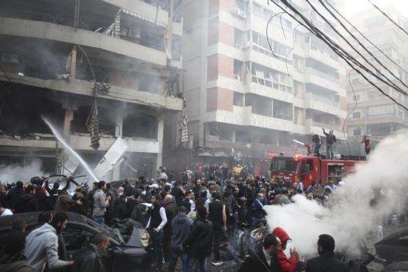 People gather as firefighters attempt to extinguish a fire at the site of an explosion in Beirut southern suburbs January 2 2014.