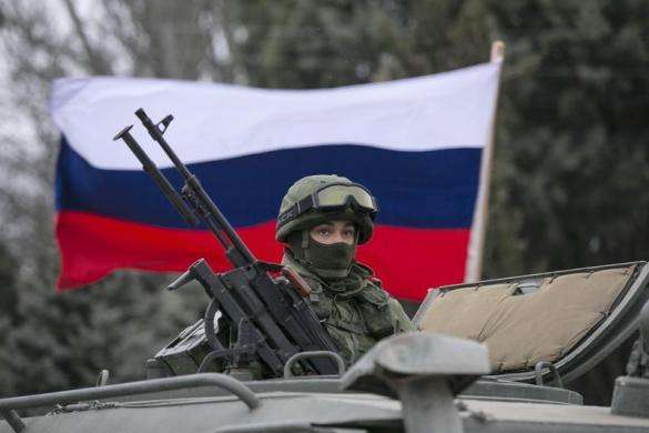 A pro-Russian holds a Russian flag behind an armed servicemen on top of a Russian army vehicle outside a Ukrainian border guard post in the Crimean town of Balaclava March 1 2014.