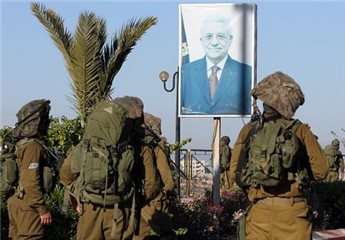 Israeli soldiers stand next to a poster of President Mahmoud Abbas during a search for three Israeli teenagers believed kidnapped by Palestinian militants, on June 18, 2014 in the West Bank village of Tapuah, west of Hebron.