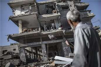 A Palestinian looks at people collecting items and belongings from a destroyed building on July 27, 2014 in the Shejaiya residential district of Gaza City as families returned to find their homes ground into rubble