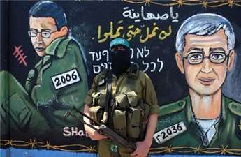 A masked Hamas fighter stands next to a mural of captured soldier Gilad Shalit during a rally in Jabaliya refugee camp in northern Gaza