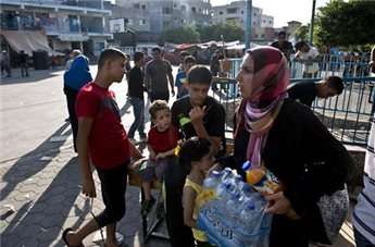 A Palestinian woman displaced from her home when fighting broke out between Israel and Hamas militants over four weeks ago, carries water bottles given to her as food handouts on Aug. 16, 2014 at a United Nations school in Jabalia