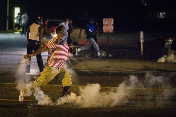A protester picks up a gas canister to throw back towards the police after tear gas was fired at demonstrators who are continuing to react to the shooting of Michael Brown in Ferguson, Missouri August 17, 2014.