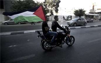 Palestinians carry the national flag as they ride through the streets of Gaza to celebrate the agreement to form a unity government on April 23, 2014