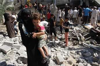 A Palestinian woman carrying a child makes her way through debris as people inspect the remains of a house following an Israeli airstrike on July 8, 2014 in the Gaza Strip town of Khan Younis.