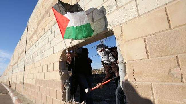 Palestinian youths appear through a hole they dug in the Israeli separation wall in the occupied West Bank on November 8, 2014.