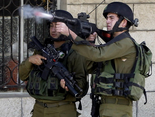 یک سرباز اسرائیلی در کرانه باختری، در حال شلیک گاز اشک آور به سمت معترضان فلسطینی است. (EPA)