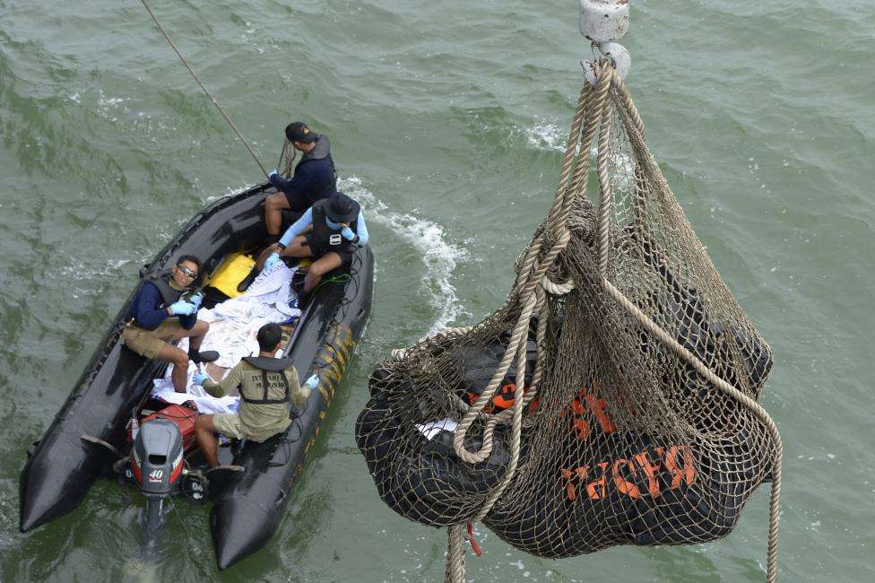 Indonesian Navy frogmen and underwater demolition unit personnel on a boat carrying bodies from AirAsia flight QZ8501, look as a body is lifted (unseen) to the Indonesian Navy vessel KRI Banda Aceh, at sea, January 3, 2015.