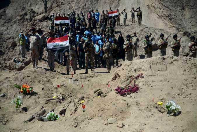 Iraqi soldiers salute as they stand next to a mass grave for Shi