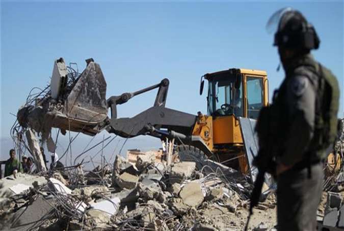 An Israeli soldier guards an area as an army bulldozer pulls down the house of a Palestinian family in Al-Dirat, near the West Bank town of Hebron (al-Khalil), January 20, 2015.