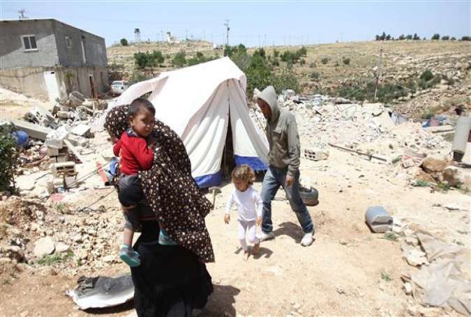 A Palestinian family, whose house was demolished by Israeli bulldozers, walk past a tent on April 21, 2015 in the southern West Bank village of Ad-Deirat Rifaiyya.