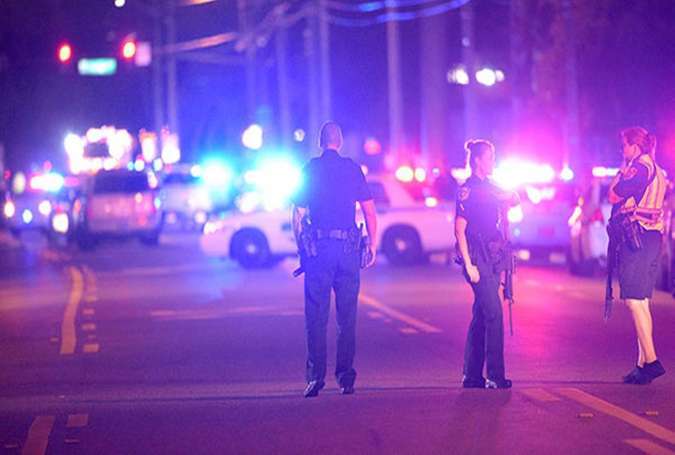 Police officers stand guard down the street from the scene of a shooting involving multiple fatalities