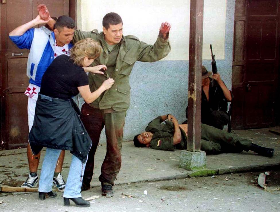 Two civilians of the town of Dolores are ordered by FARC guerrillas to search a Colombian policeman's clothes for concealed weapons during a siege of the town in Colombia's central Tolima province, November 1999. A fellow wounded policeman lies in the ba