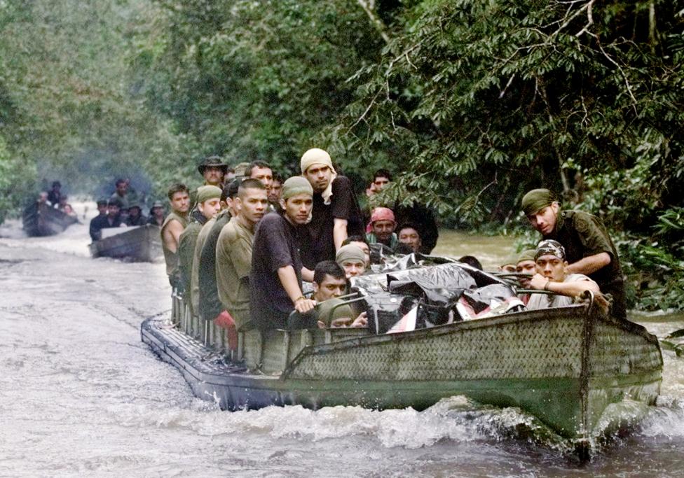 46 Colombian police held prisoner by FARC rebels huddle in a boat as they are escorted by guerrillas from behind, near the end of a two-day river journey on their way to being freed in a unilateral release, June 2001.