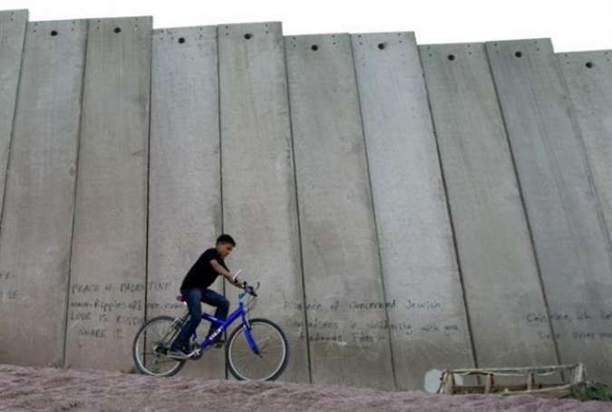 A Palestinian youth rides his bicycle next to Israel