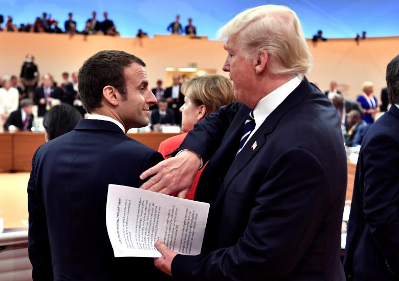 U.S. President Donald Trump claps the shoulder of French President Emmanuel Macron at the start of the first working session.