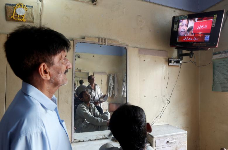 Men look at a television screen displaying the coverage of Pakistan's Supreme Court's decision on disqualifying Pakistan's Prime Minister Nawaz Sharif, at a barber shop in Karachi.