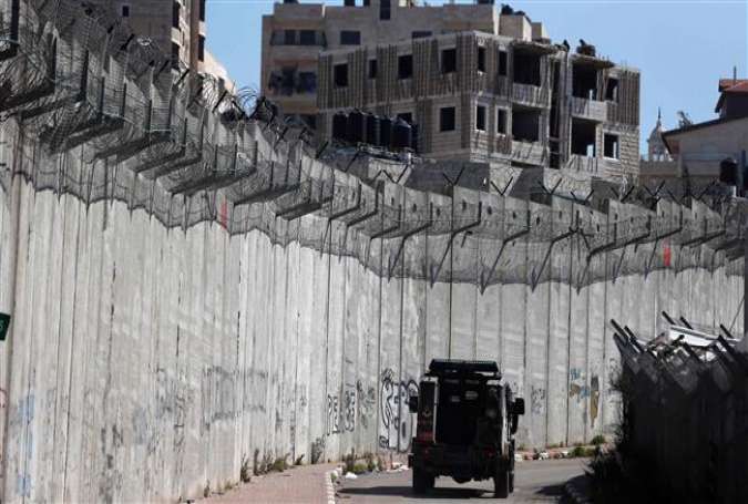 An Israeli police car patrols along a section of Israel’s Apartheid Wall that separates the West Bank city of al-Ram (L) from east al-Quds (Jerusalem) (R)