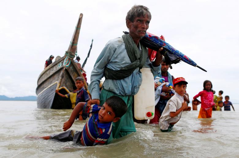 A Rohingya refugee man pulls a child as they walk to the shore after crossing the Bangladesh-Myanmar border by boat through the Bay of Bengal in Shah Porir Dwip, Bangladesh.