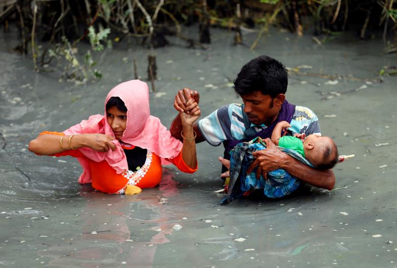 Rohingya refugees carry their child as they walk through water after crossing border by boat through the Naf River in Teknaf, Bangladesh.