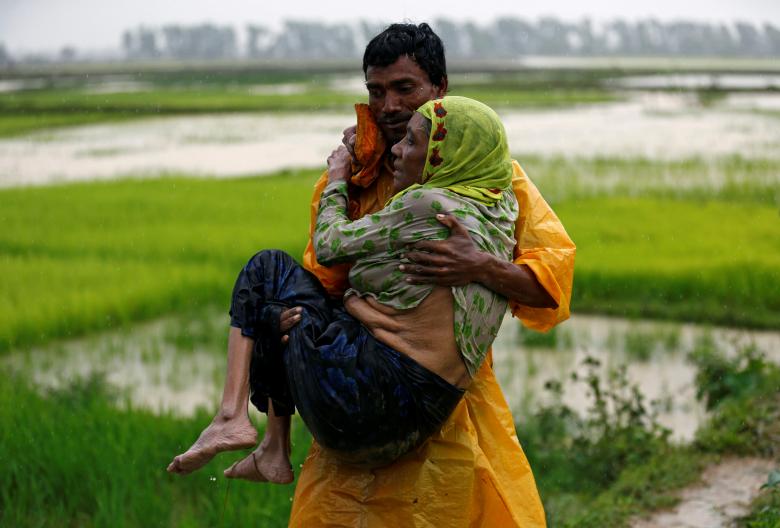 A local man carries an old Rohingya refugee woman as she is unable to walk after crossing the border, in Teknaf, Bangladesh.