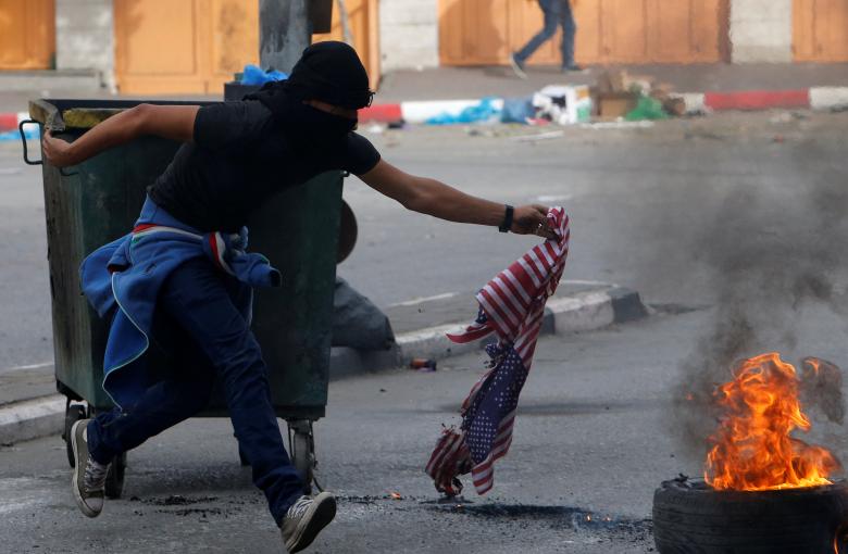 A Palestinian demonstrator burns a U.S. flag during clashes with Israeli troops at a protest as Palestinians call for a 