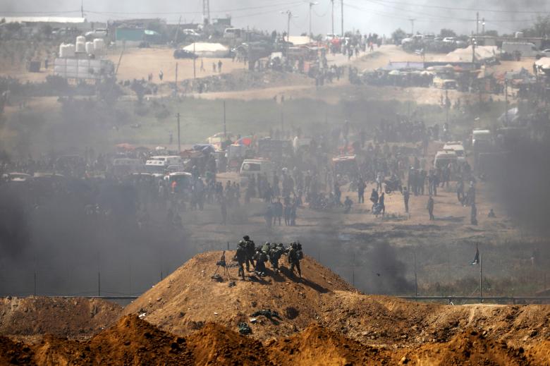 Israeli soldiers are seen next to the border fence on the Israeli side of the Israel-Gaza border as Palestinians protest on the Gaza side of the border April 6, 2018.