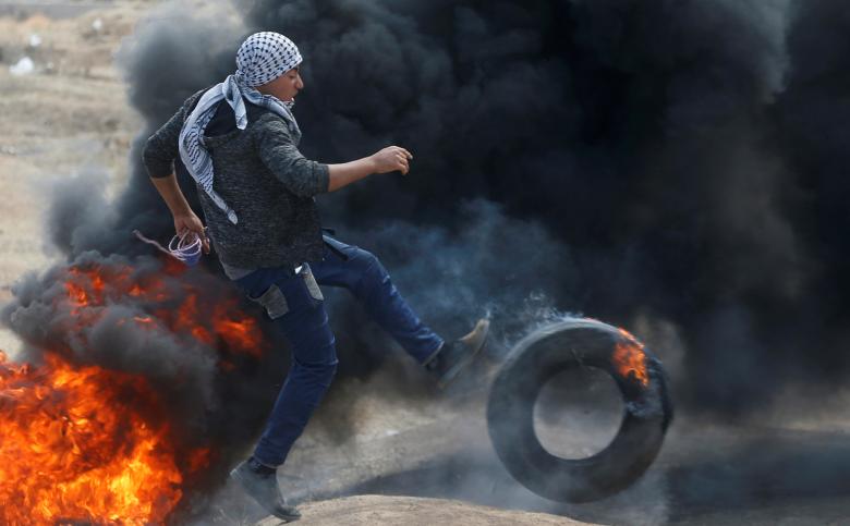 A Palestinian demonstrator kicks a burning tire during a protest against U.S. embassy move to Jerusalem and ahead of the 70th anniversary of Nakba, at the Israel-Gaza border, east of Gaza City.