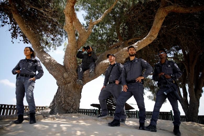 An Israeli police officer uses binoculars as he sits on a tree, as other police personnel stand close to the Israeli side of the border with the Gaza Strip, Israel.