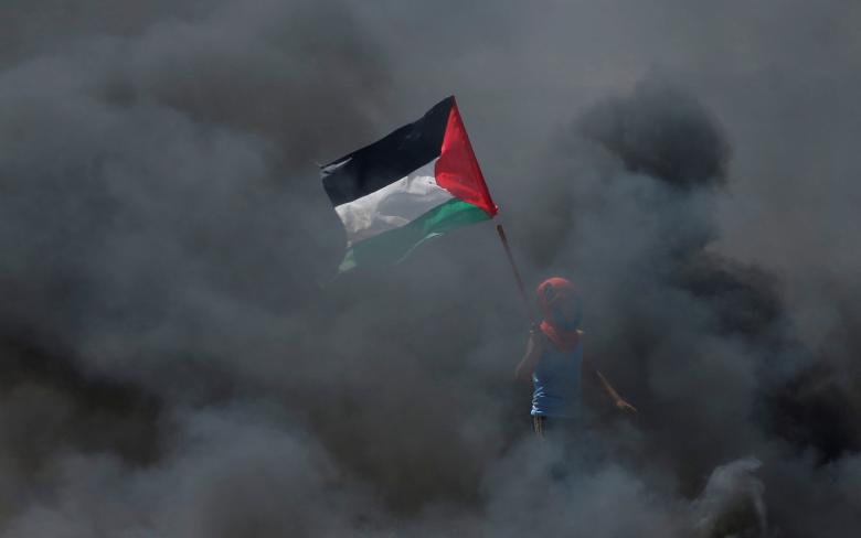 A boy holds a Palestinian flag as he stands amidst smoke during a protest against U.S. embassy move to Jerusalem and ahead of the 70th anniversary of Nakba, at the Israel-Gaza border east of Gaza City.
