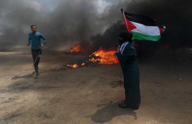 A woman holds a Palestinian flag as a demonstrator runs during a protest against U.S. embassy move to Jerusalem and ahead of the 70th anniversary of Nakba, at the Israel-Gaza border in the southern Gaza Strip.