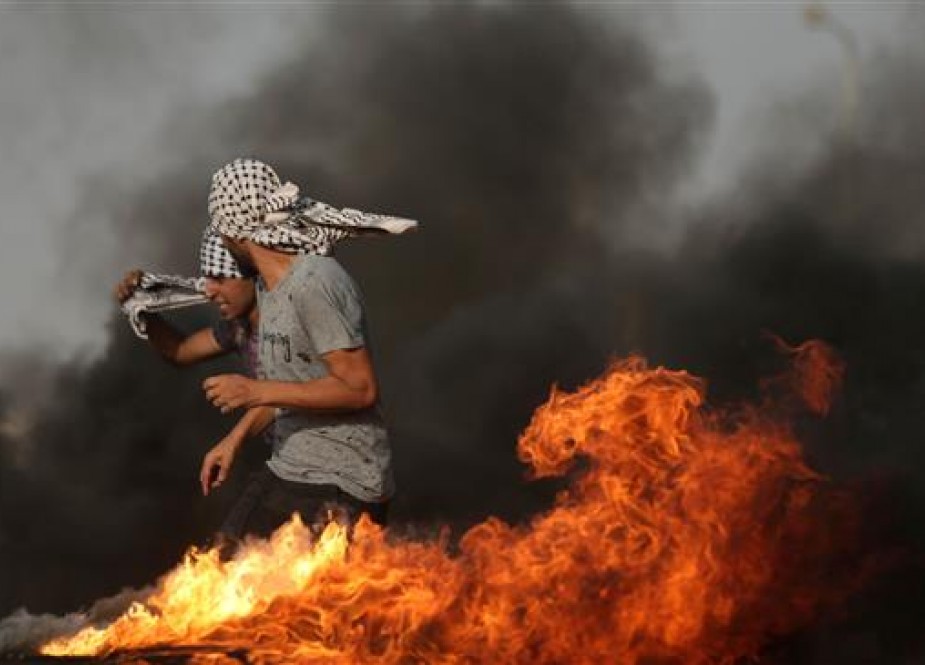 A Palestinian demonstrator walks in the smoke billowing from burning tyres during clashs with Israeli forces along the border with the Gaza Strip, on May 18, 2018. (Photo by AFP)