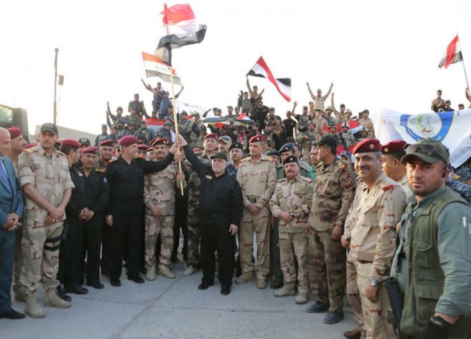 Iraqi Prime Minister Haidar al-Abadi (C) holds an Iraqi flag as he announces victory over ISIL.jpg