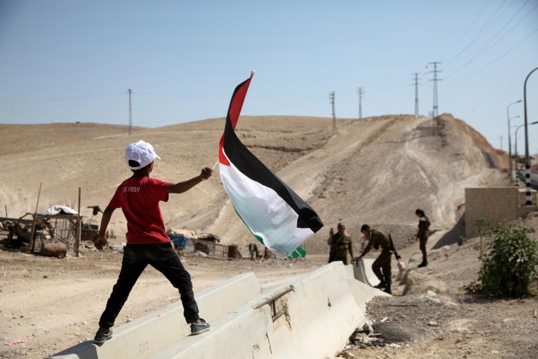 A Palestinian Bedouin boy waves a Palestinian flag in front of Israeli soldiers at al-Khan al-Ahmar near Jericho in the occupied West Bank.