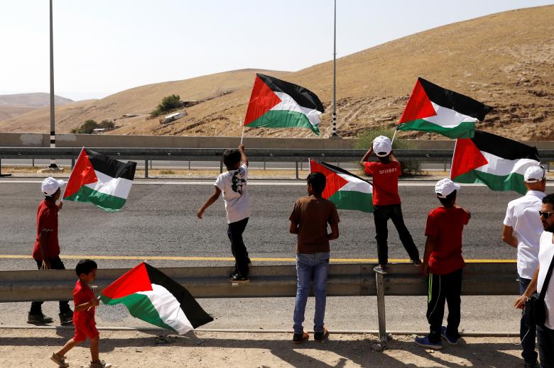 Palestinian Bedouin boys wave Palestinian flags on a main road leading from Jerusalem to the Dead sea at the al-Khan al-Ahmar near Jericho in the occupied West Bank.