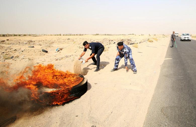 Iraqi policemen throw sand to put out a fire set by protesters, during a protest at the main entrance to the giant Zubair oilfield near Basra, July 17.