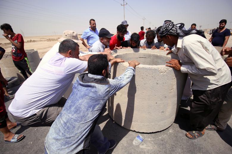 Iraqi protesters push concrete blocks to block the road during a protest in south of Basra, July 16.