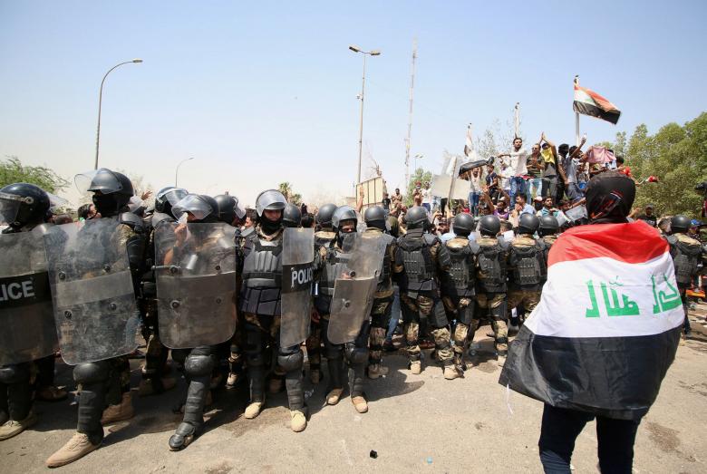 A protester wears an Iraqi flag in front of security forces during a protest near the main provincial government building in Basra, July 15.